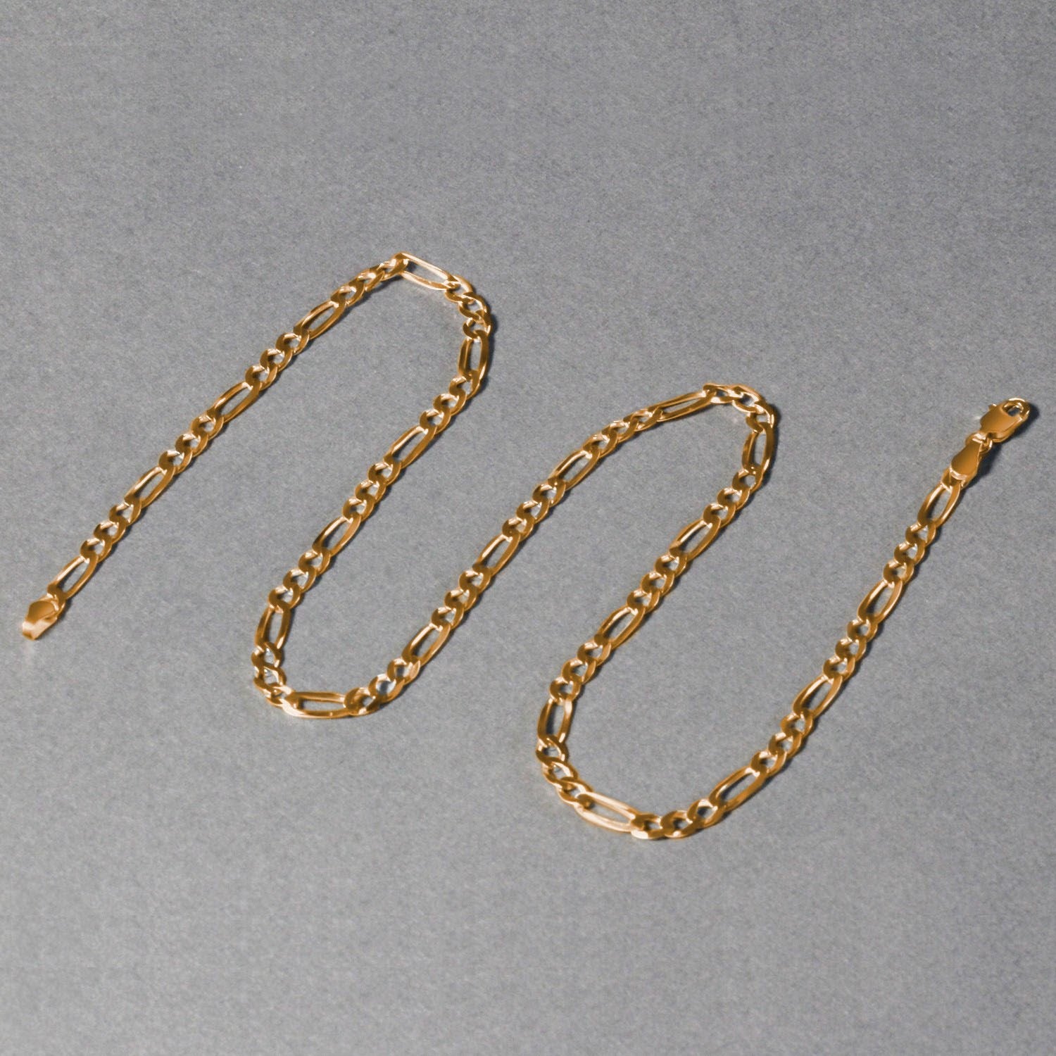 14K yellow gold solid Figaro chain, 3.80mm, arranged in an S‑shape on a white background to highlight polished long‑and‑short links and solid gold craftsmanship.