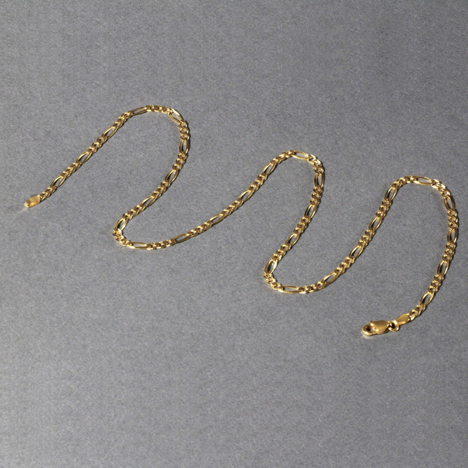 10K yellow gold solid Figaro chain, 2.60mm, arranged in a flat S‑shape to highlight polished long‑and‑short links and solid gold craftsmanship.